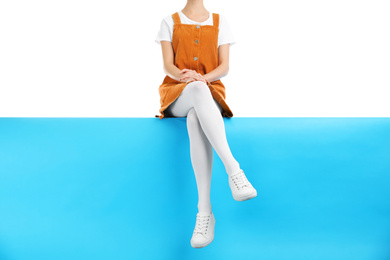 Woman wearing white tights and stylish shoes sitting on color background, closeup