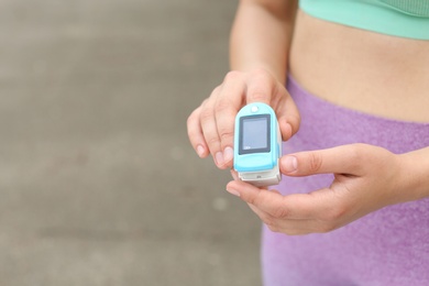 Young woman checking pulse with medical device after training on street, closeup. Space for text