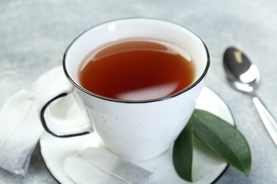 Photo of Aromatic tea in cup, teabags and green leaves on grey table, closeup