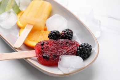 Plate of delicious popsicles, ice cubes and fresh fruits on white table