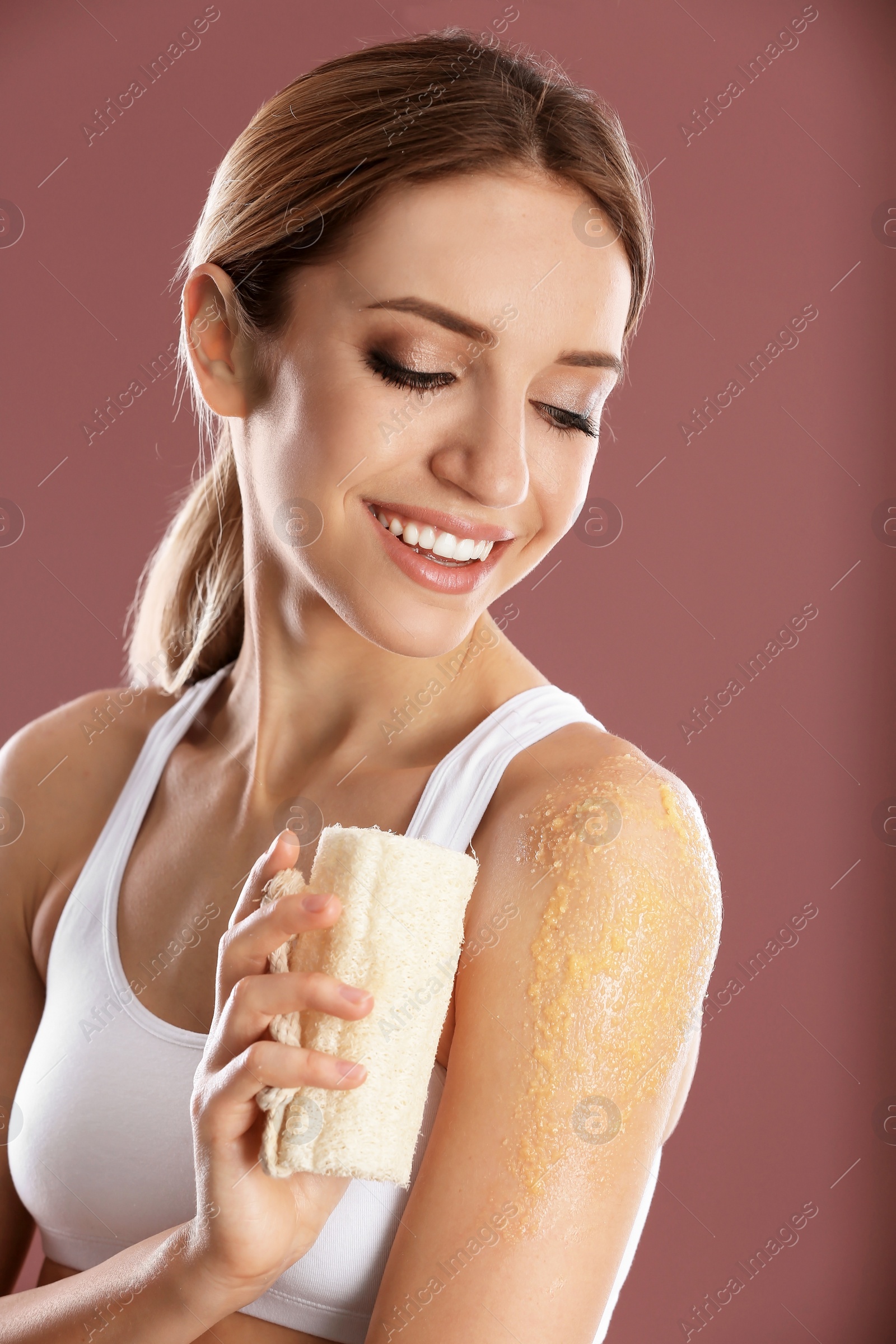 Photo of Young woman applying natural scrub on her shoulder against color background