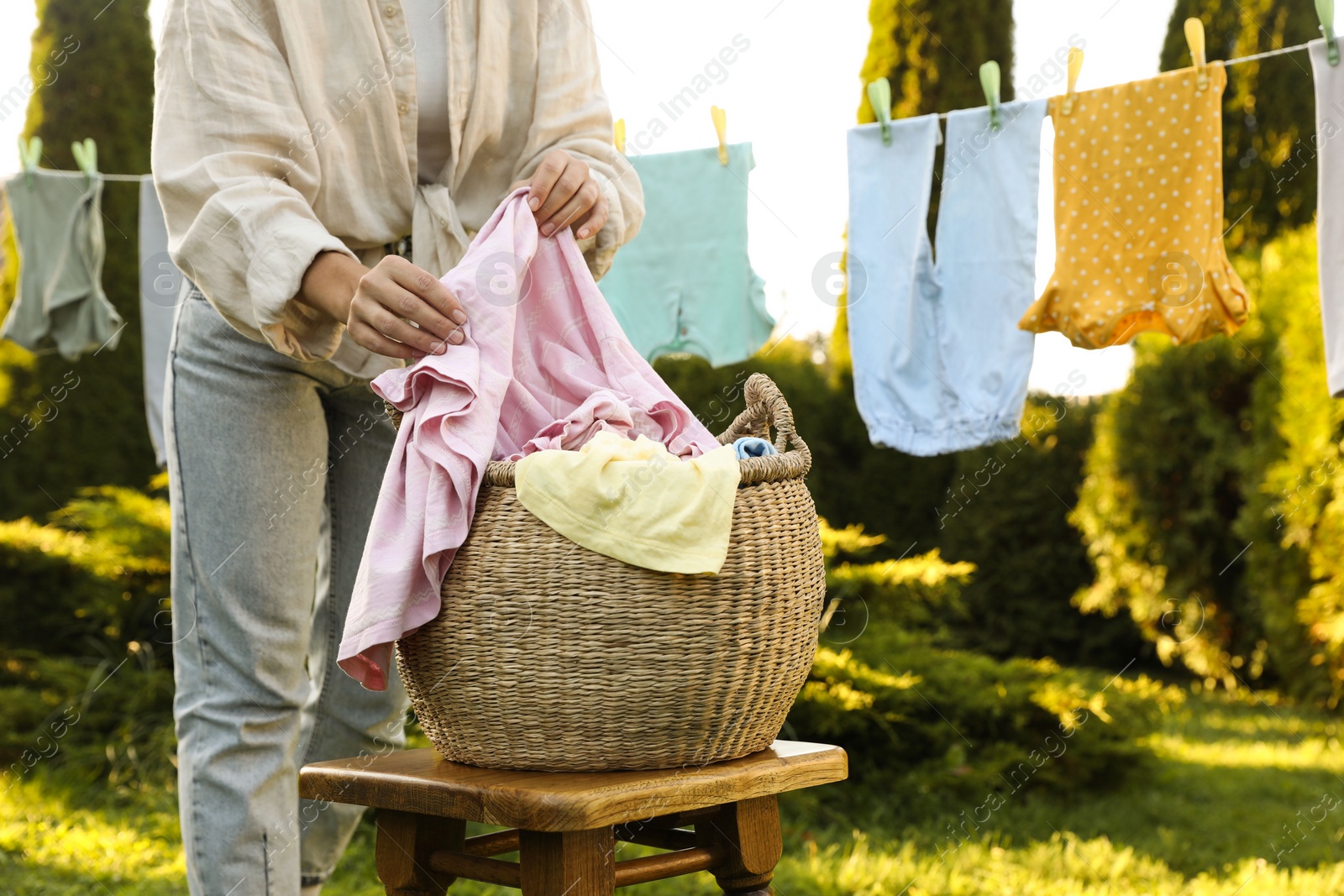 Photo of Woman hanging baby clothes with clothespins on washing line for drying in backyard, closeup