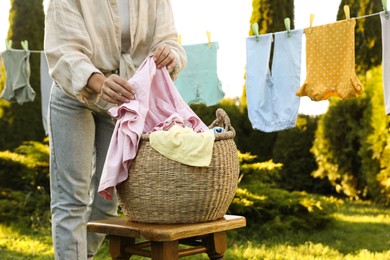 Woman hanging baby clothes with clothespins on washing line for drying in backyard, closeup