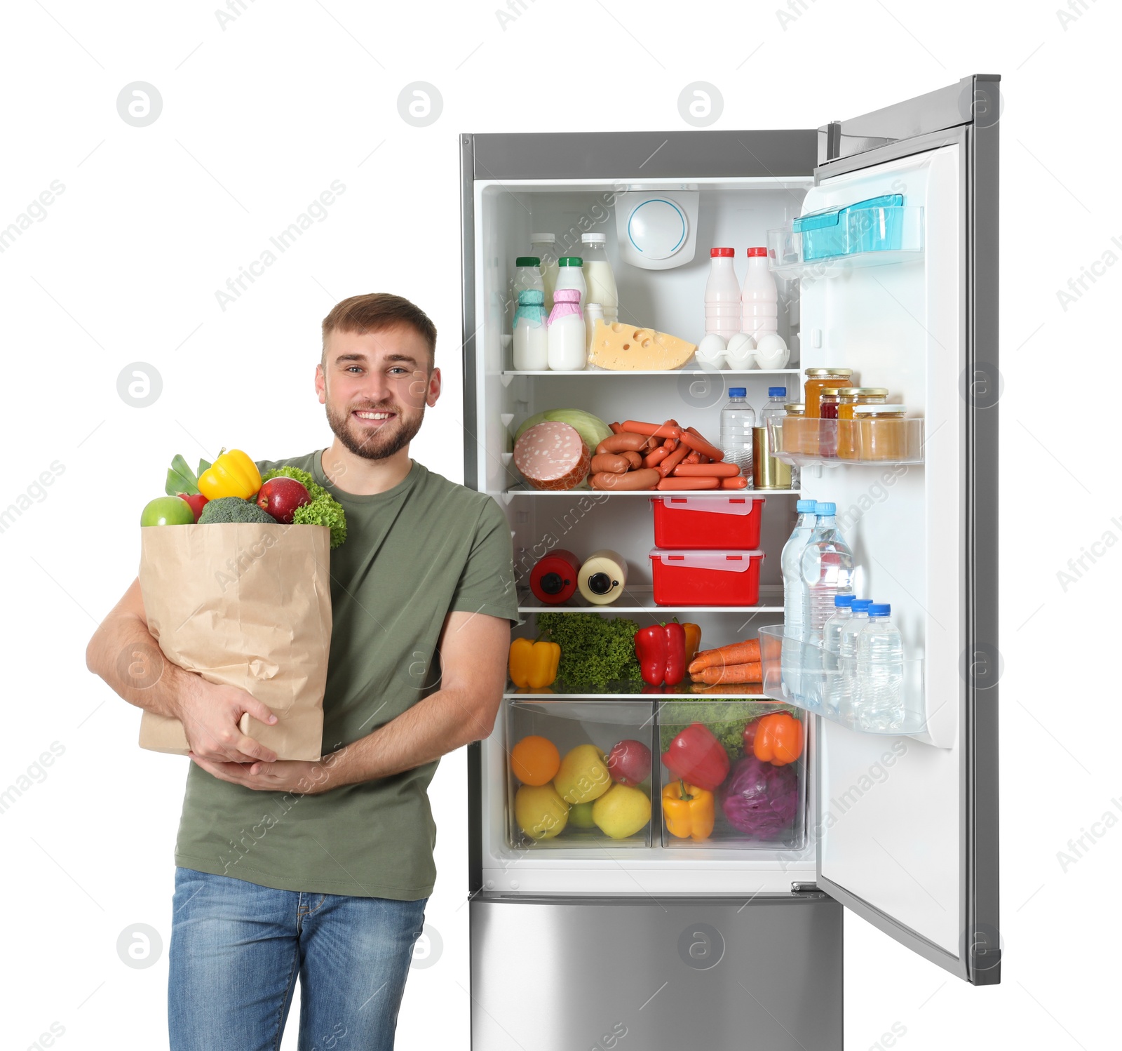 Photo of Young man with bag of groceries near open refrigerator on white background