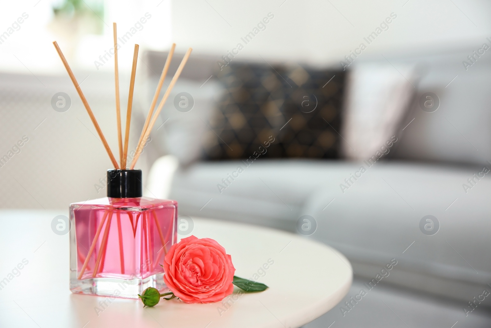Photo of Aromatic reed air freshener and rose on table indoors