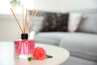 Photo of Aromatic reed air freshener and rose on table indoors