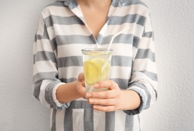 Photo of Young woman holding glass with lemon cocktail against light background