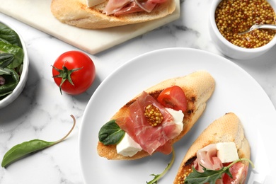 Photo of Delicious bruschettas with prosciutto served on marble table, flat lay