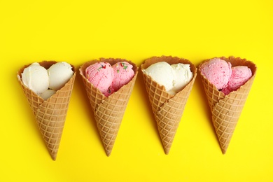 Photo of Delicious ice creams in wafer cones on yellow background, flat lay