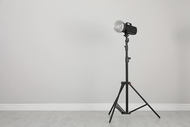 Studio flash light with reflector on tripod near grey wall in room, space for text. Professional photographer's equipment