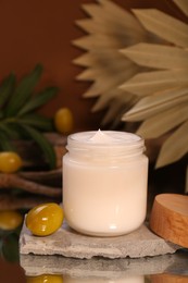 Photo of Jar of cream and olives on glass table