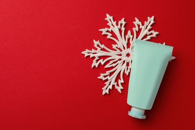 Photo of Tube of hand cream and snowflake on red background, flat lay with space for text. Winter skin care