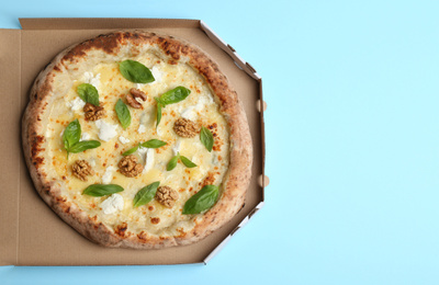 Photo of Delicious cheese pizza with walnuts and basil in takeout box on light blue background, top view