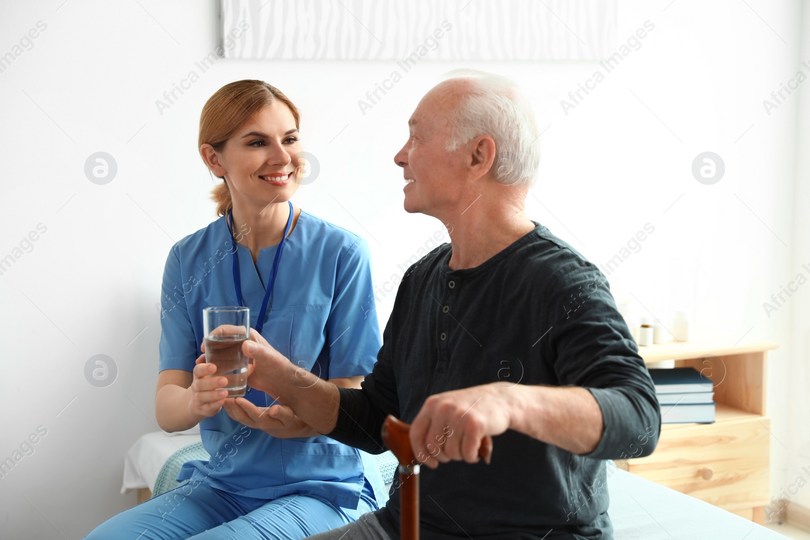 Photo of Nurse giving glass of water to elderly man indoors. Medical assistance