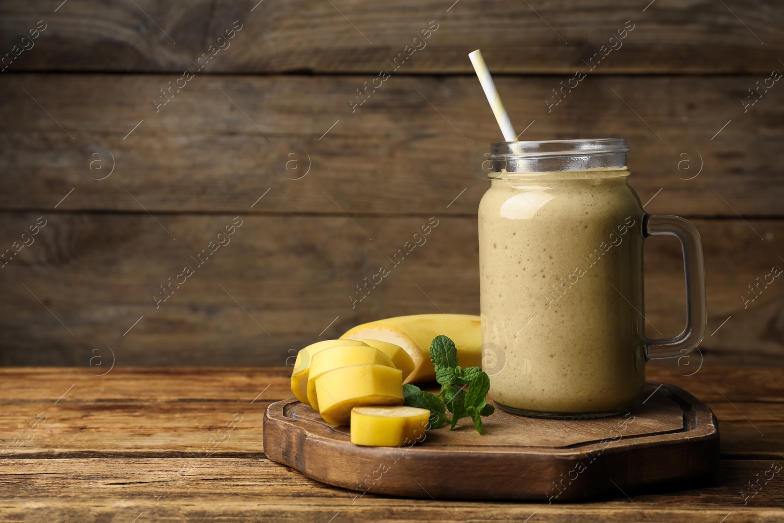 Photo of Mason jar with delicious fruit smoothie and fresh banana on wooden table. Space for text