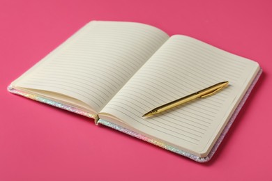 Stylish open notebook with blank sheets and pen on pink background