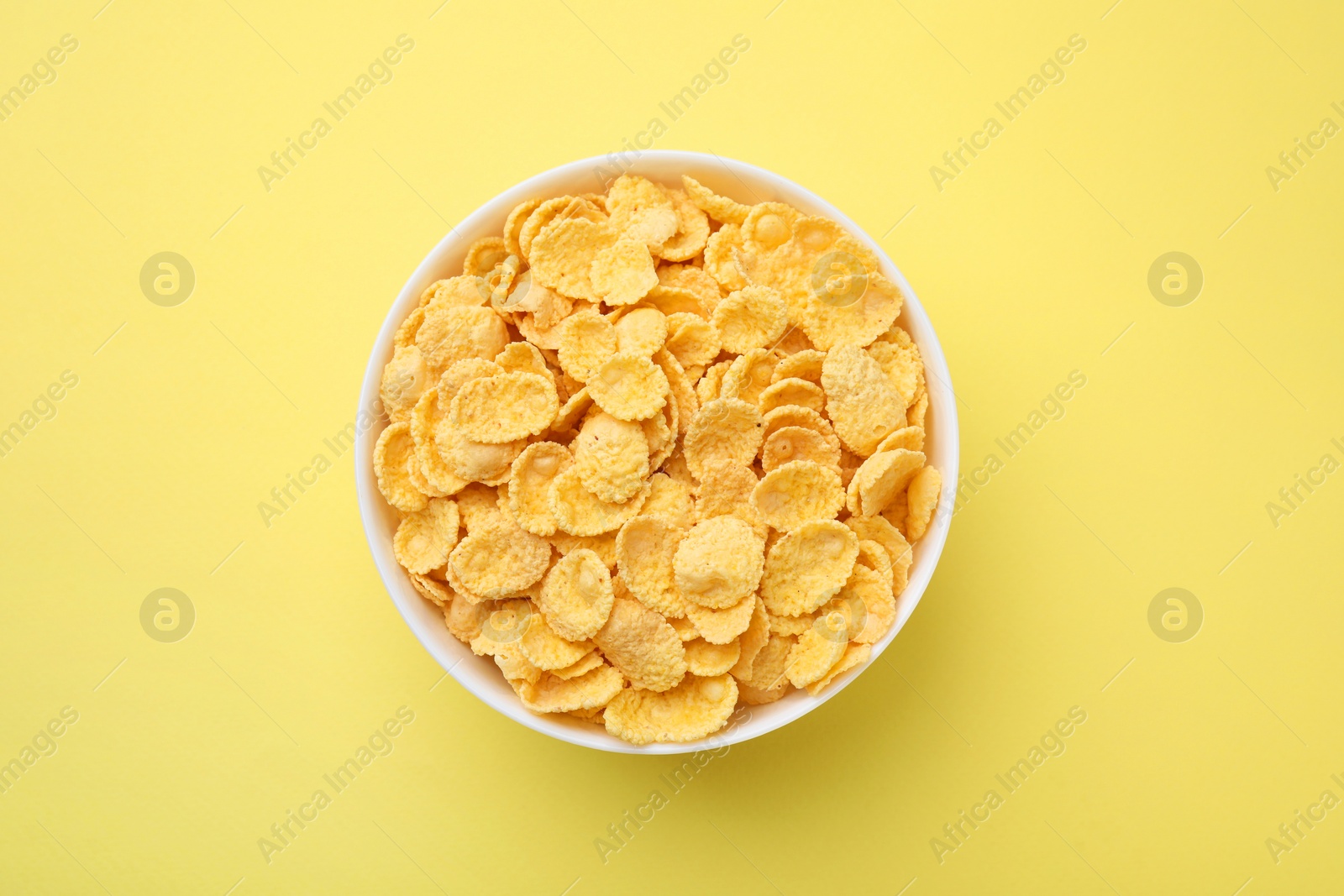 Photo of Breakfast cereal. Tasty corn flakes in bowl on yellow table, top view