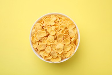 Breakfast cereal. Tasty corn flakes in bowl on yellow table, top view