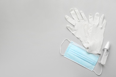 Medical gloves, protective mask and hand sanitizer on grey background, flat lay. Space for text