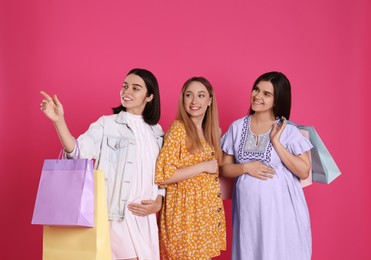 Photo of Happy pregnant women with shopping bags on pink background