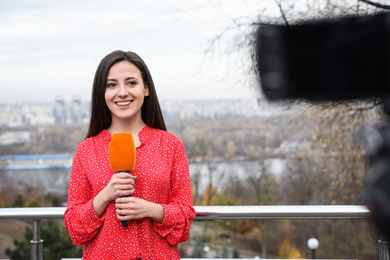 Young female journalist with microphone working on city street