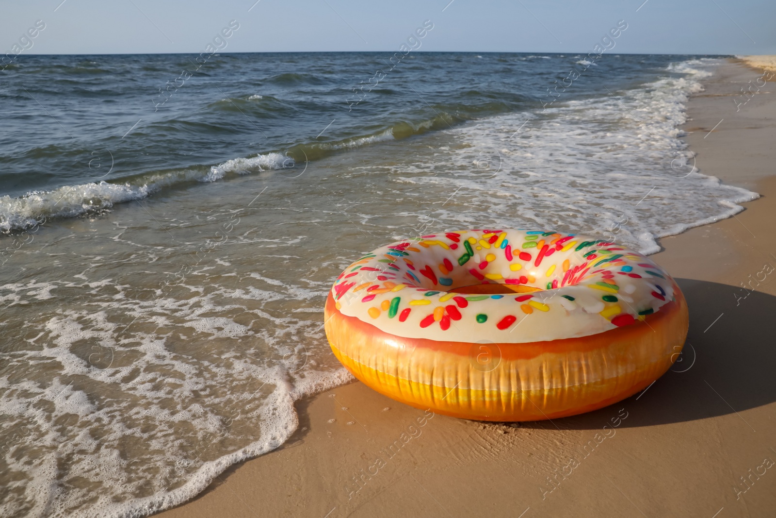 Photo of Inflatable ring with doughnut pattern on sandy beach near sea, space for text