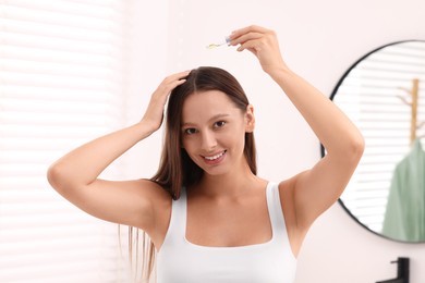 Photo of Beautiful woman applying serum onto hair indoors