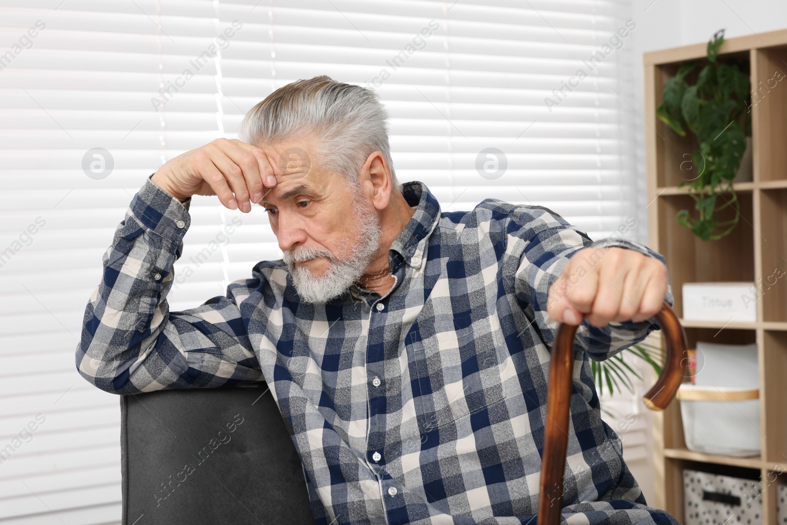 Photo of Senior man with walking cane sitting on armchair at home