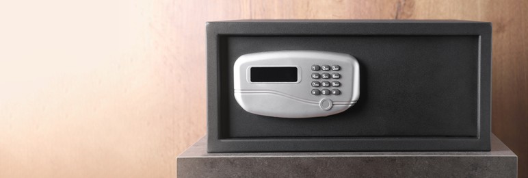 Image of Black steel safe with electronic lock on grey table, space for text. Banner design
