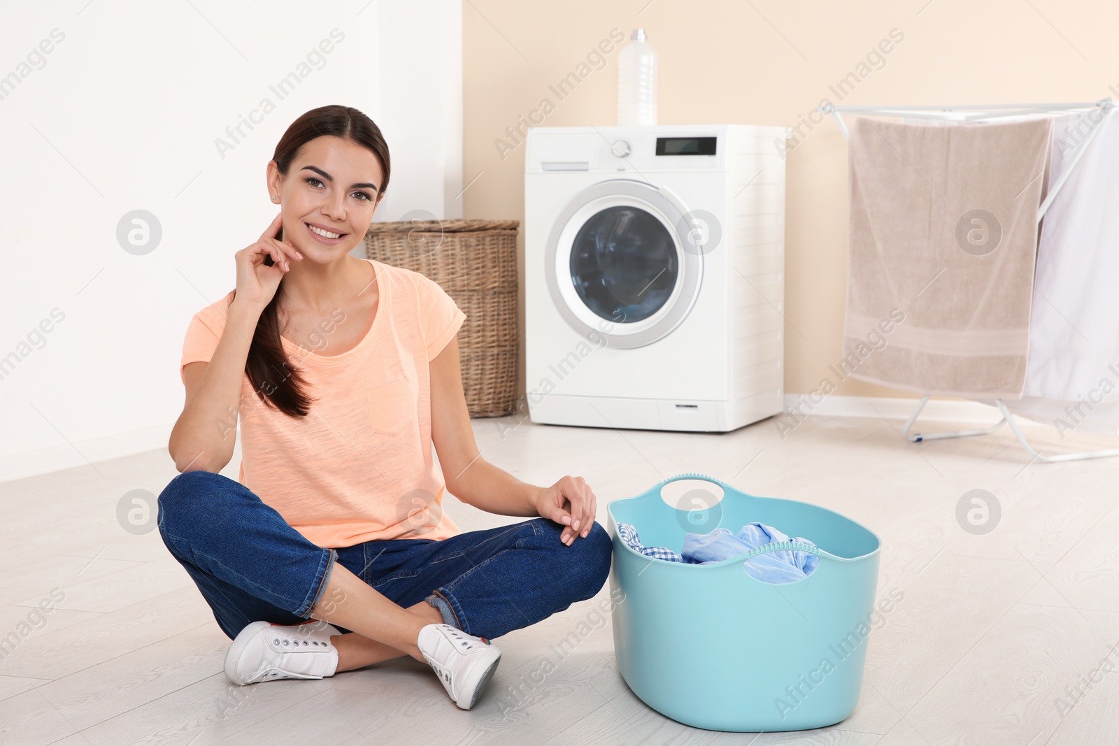 Photo of Young woman with laundry basket near washing machine at home