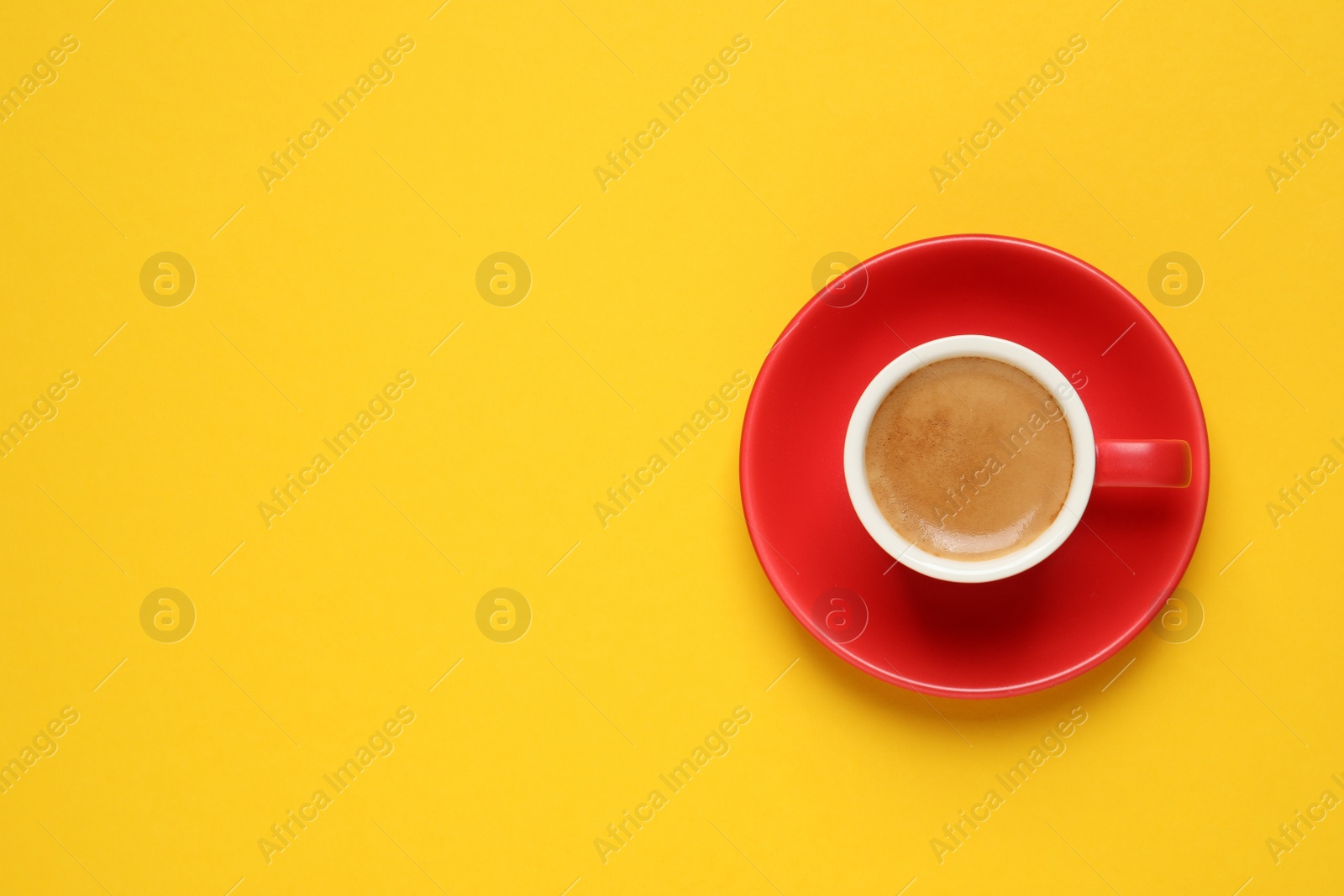 Photo of Aromatic coffee in red cup on yellow background, top view. Space for text