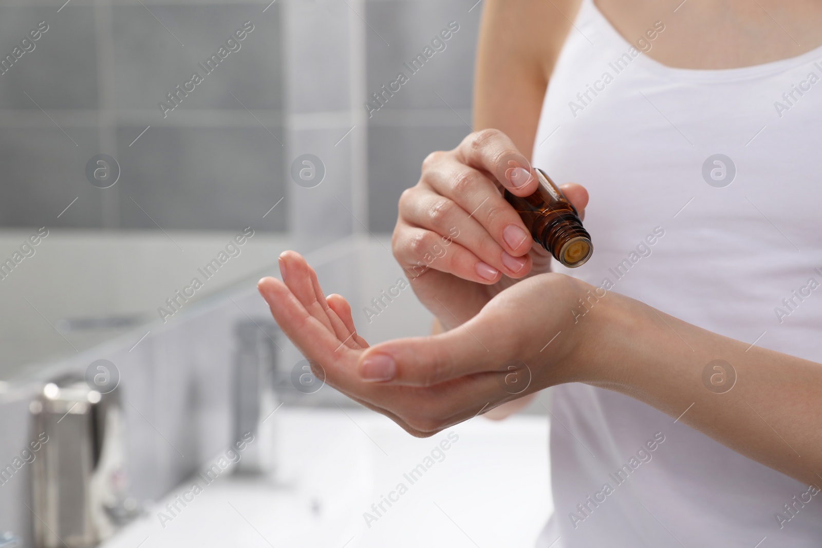 Photo of Young woman applying essential oil onto wrist in bathroom, closeup