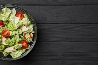 Photo of Bowl of delicious salad with Chinese cabbage, cucumber and tomatoes on black wooden table, top view. Space for text