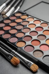 Photo of Beautiful eye shadow palette and brushes on dark grey table