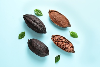 Photo of Cocoa pods with beans and powder on light blue background, flat lay
