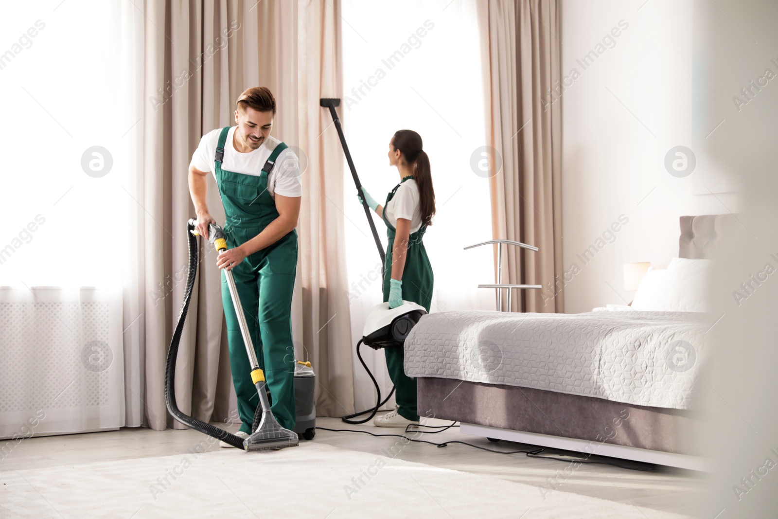 Photo of Team of janitors cleaning bedroom with professional equipment