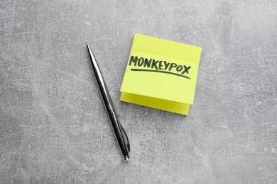 Paper note with word Monkeypox and pen on light grey table, flat lay
