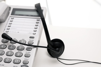 Photo of Headset and desk phone on table, space for text. Technical support concept