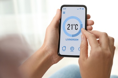 Woman using smartphone to control heating system in house, closeup