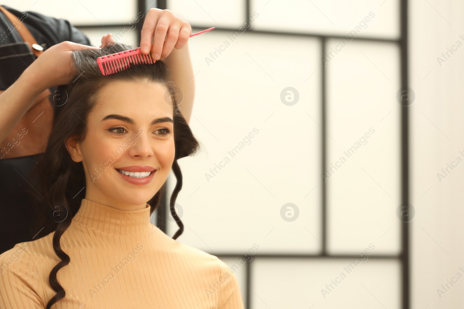 Photo of Professional hairdresser combing woman's hair indoors, closeup. Space for text