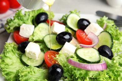 Photo of Dressing tasty fresh Greek salad with olive oil, closeup