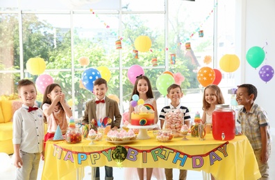 Photo of Cute children near table with treats at birthday party indoors