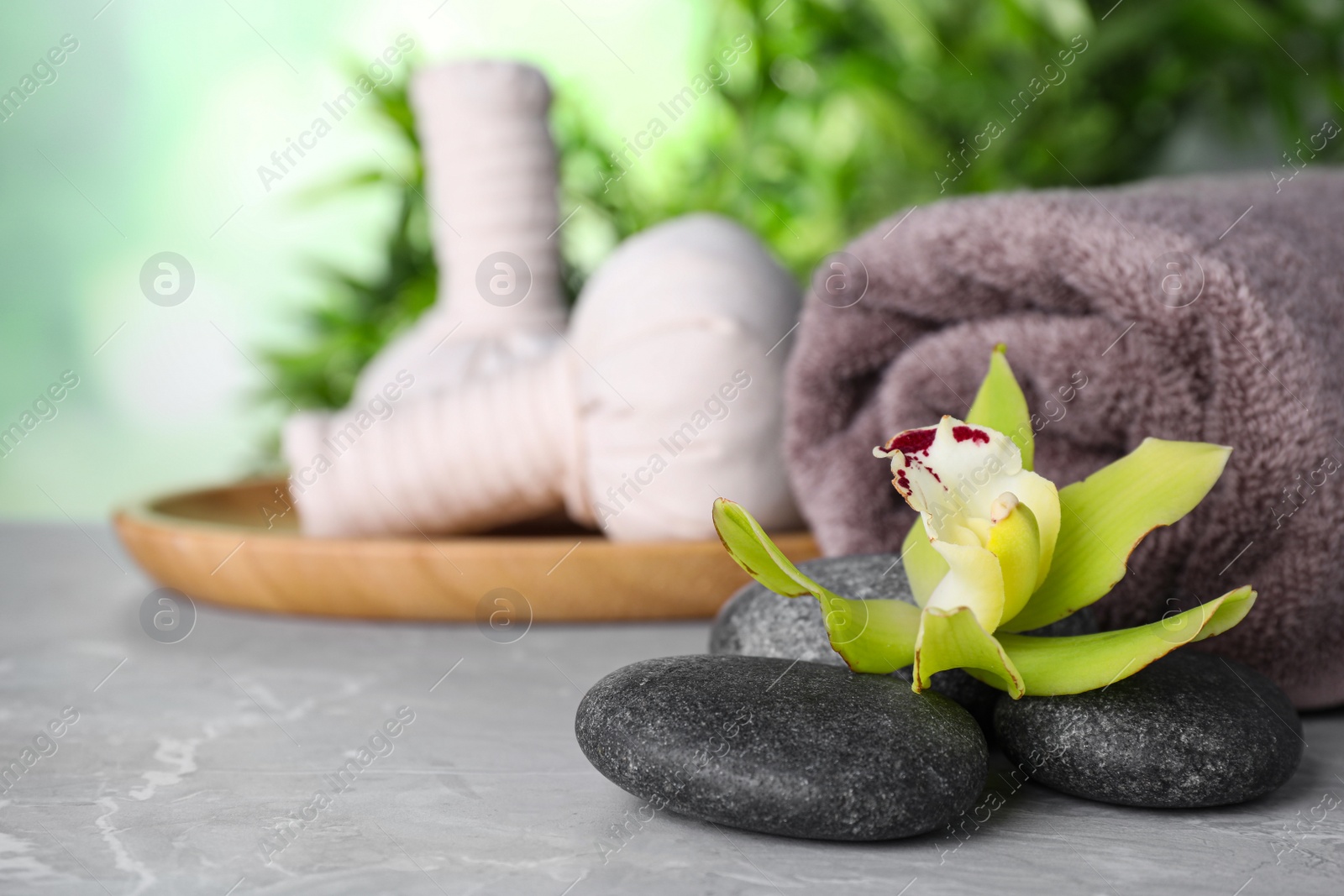 Photo of Spa stones, exotic flower, towel and herbal bags on grey marble table, space for text