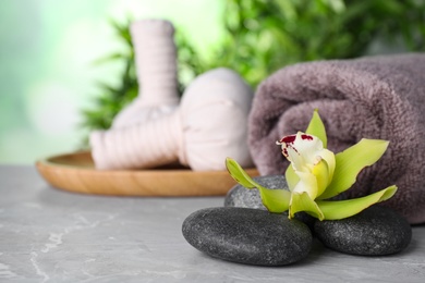 Spa stones, exotic flower, towel and herbal bags on grey marble table, space for text