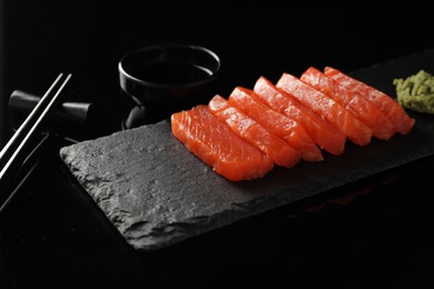 Photo of Delicious salmon sashimi, wasabi, soy sauce and chopsticks on black mirror surface