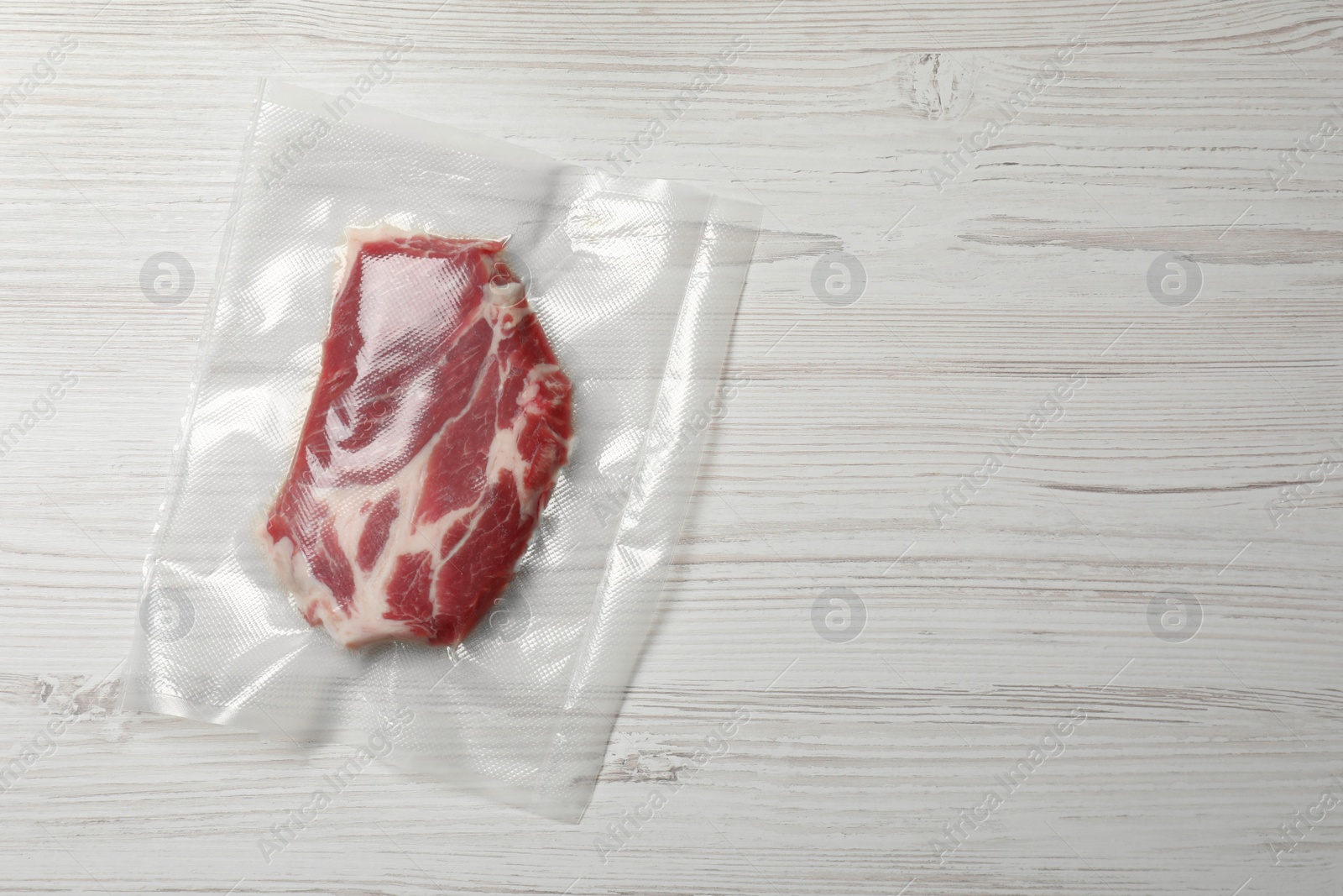 Photo of Raw beef in vacuum pack on white wooden table, top view. Space for text