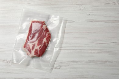 Photo of Raw beef in vacuum pack on white wooden table, top view. Space for text