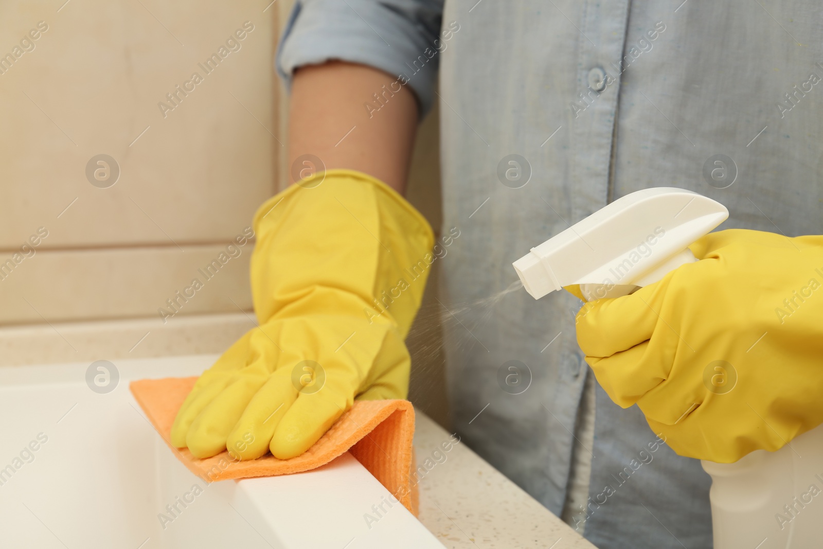 Photo of Woman cleaning sink with detergent and rag in bathroom, closeup