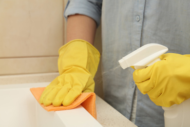 Photo of Woman cleaning sink with detergent and rag in bathroom, closeup