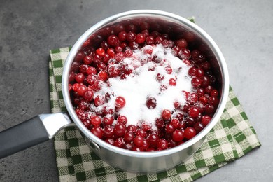 Photo of Making cranberry sauce. Fresh cranberries with sugar in saucepan on gray table, closeup